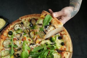 Close-up of a fresh veggie pizza with arugula, olives, and zucchini, ready to eat.